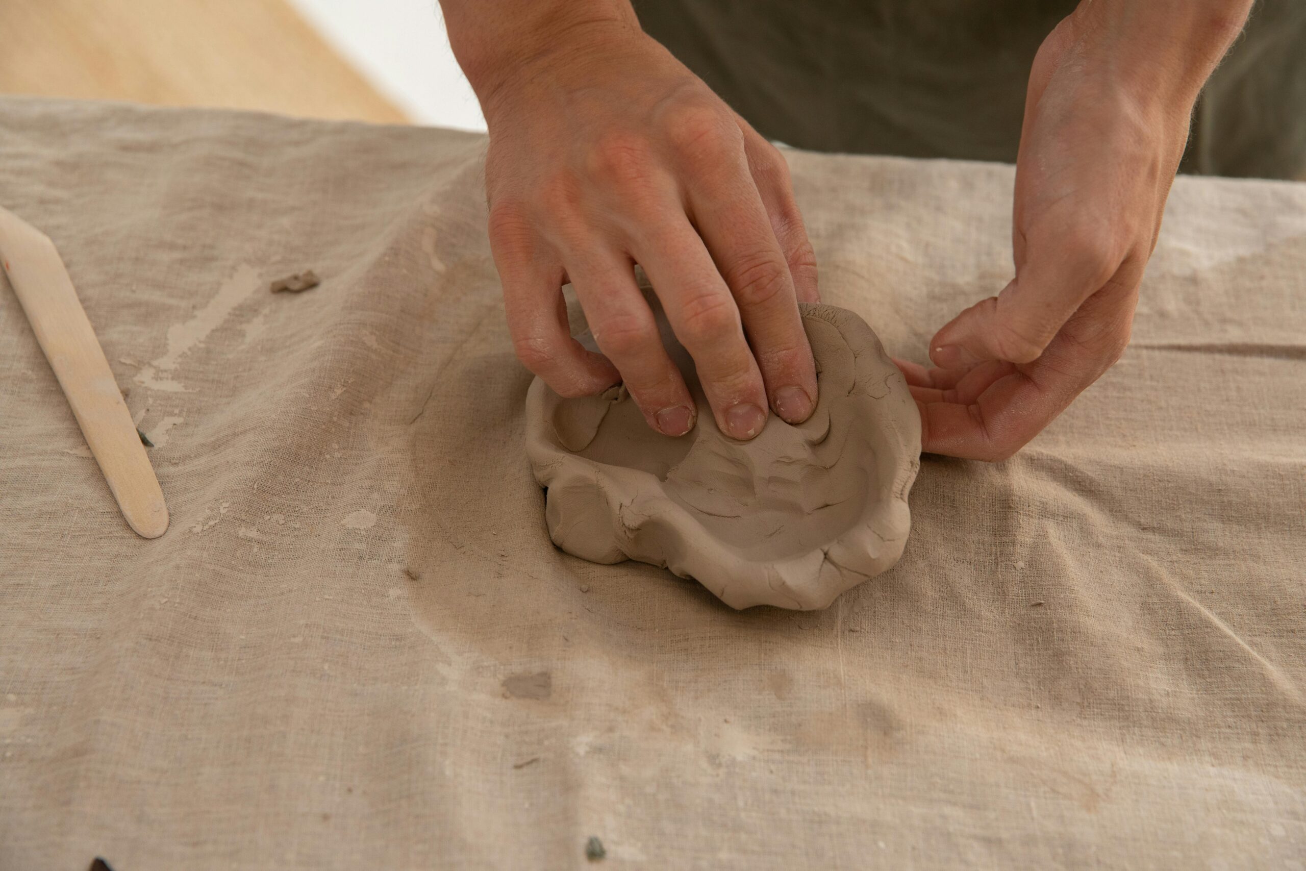 From above of crop anonymous ceramist standing at table and creating handmade product from clay in creative studio in daylight